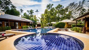 A circular pool with blue tiles, surrounded by lounge chairs and umbrellas, with a building and tropical vegetation in the background. - Anahata Resort Samui (Koh Samui)
