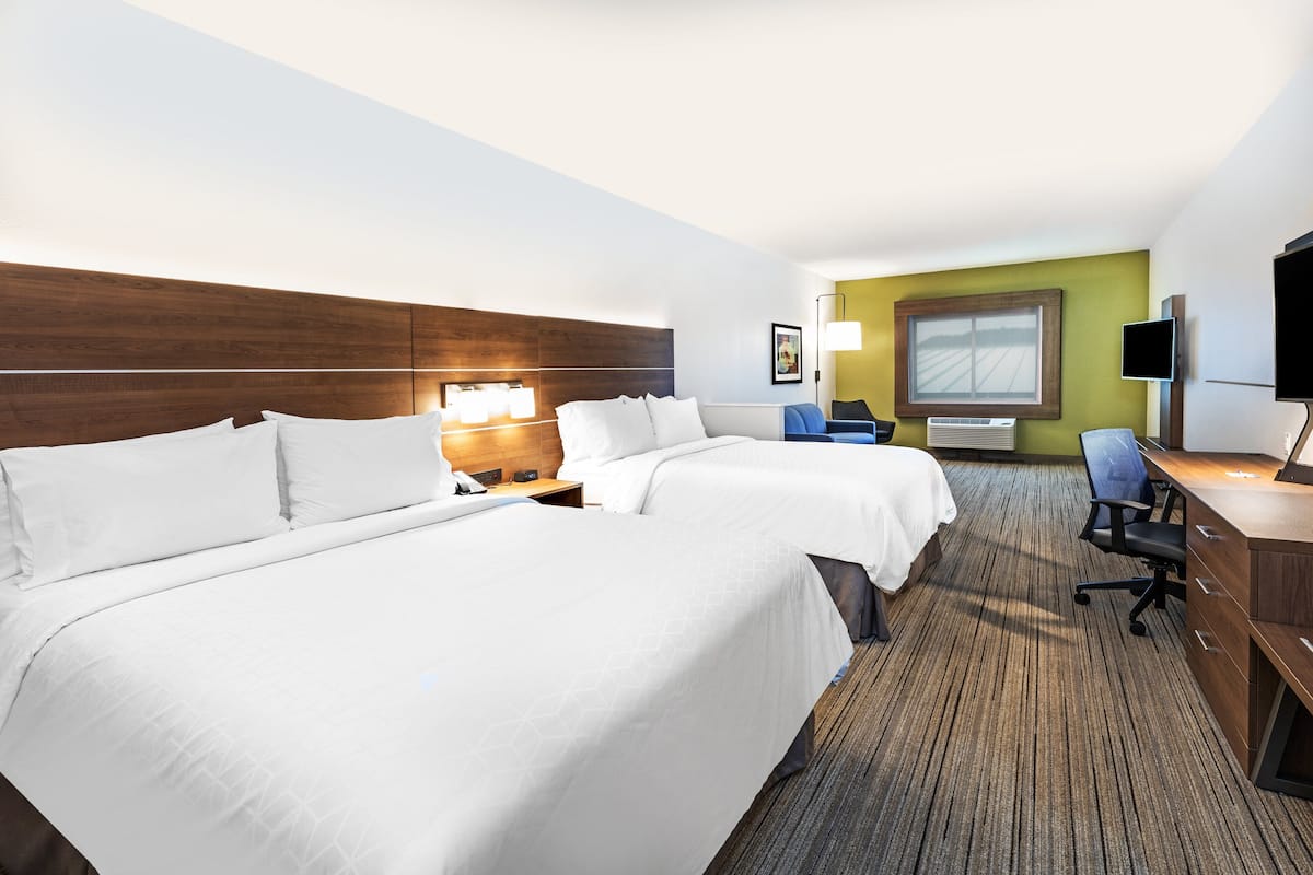 A hotel room with two beds, a desk, a chair, a TV, and a window with a view.