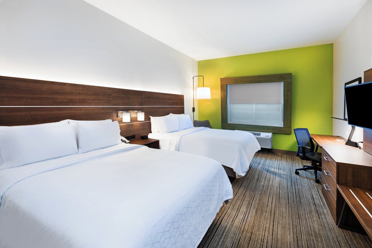 A hotel room with two beds, a desk, a chair, a TV, and a large window.