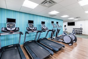 Un gimnasio con cintas de correr, elípticas y un soporte para pesas.
