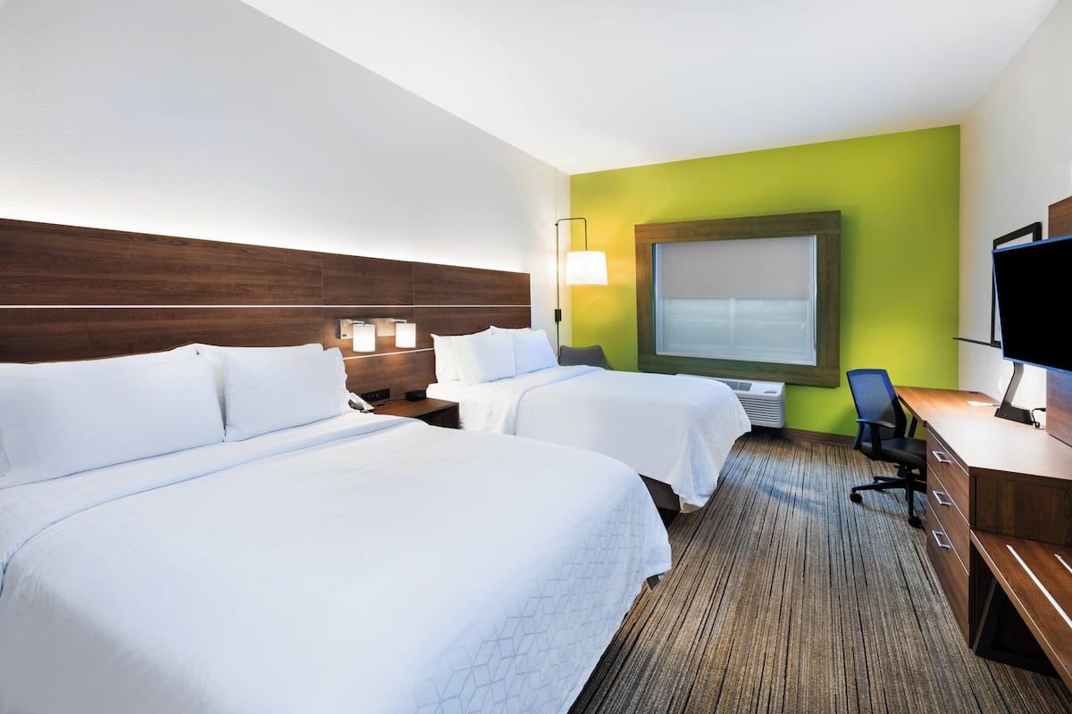 A hotel room with two beds, a desk, a chair, a TV, and a large window.