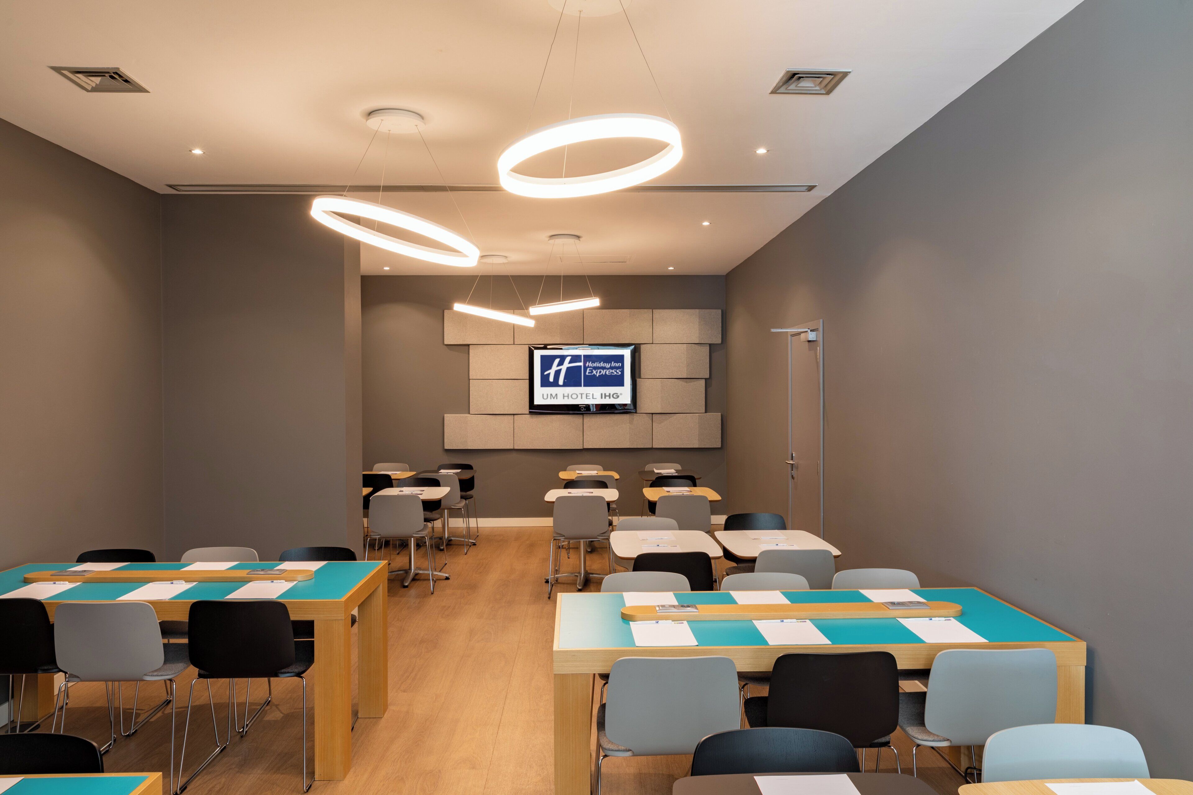 A conference room with tables and chairs, a television screen, and modern lighting fixtures.