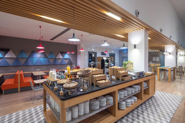 A modern breakfast area with a buffet setup, seating, and a wooden ceiling design.