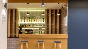 A bar area with a wooden counter, three stools, and shelves stocked with bottles and glasses. - Holiday Inn Express Porto - Exponor by IHG (Matosinhos)