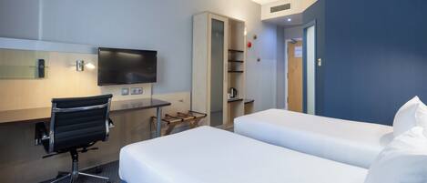 A hotel room with a desk, two beds, a TV, and a wardrobe.