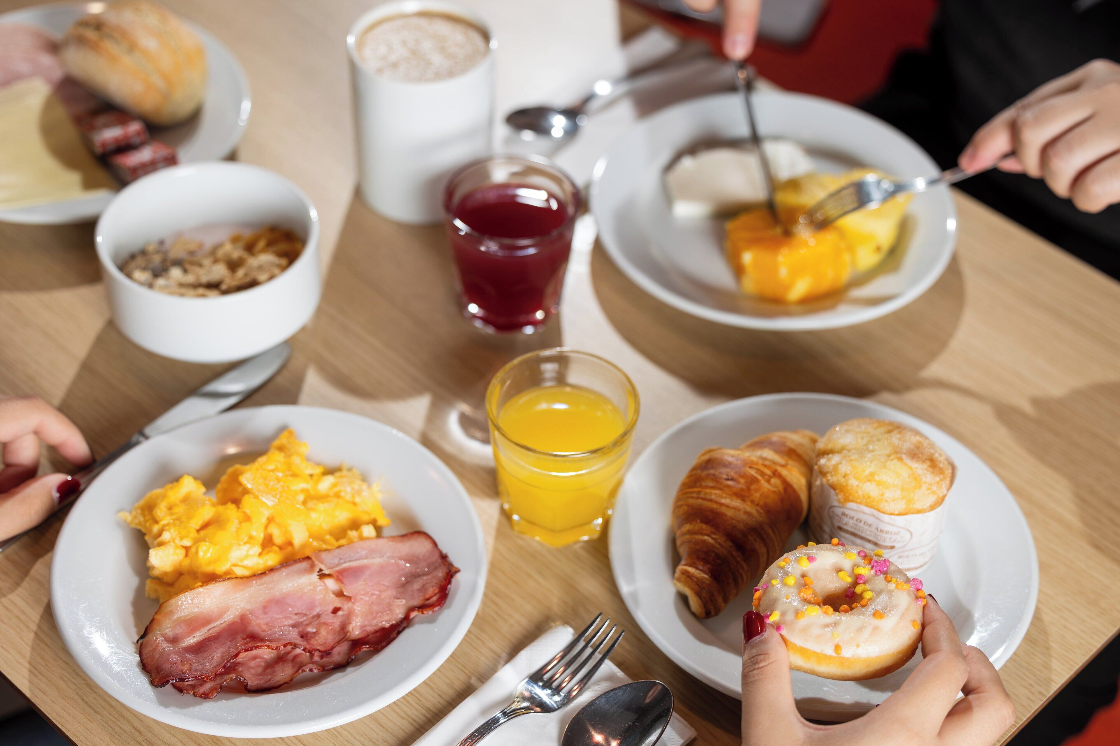 A breakfast setting with plates of eggs, bacon, and pastries, along with a glass of orange juice.