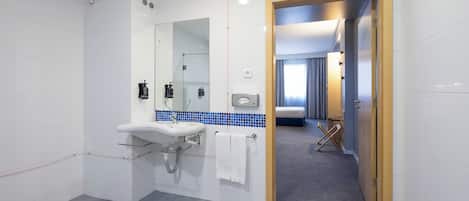 Casa de banho moderna com lavatório, espelho e porta-toalhas. Uma zona de duche é visível ao fundo.