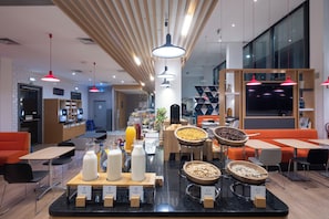 A modern breakfast area with a variety of food options, seating arrangements, and a visible kitchen area in the background.