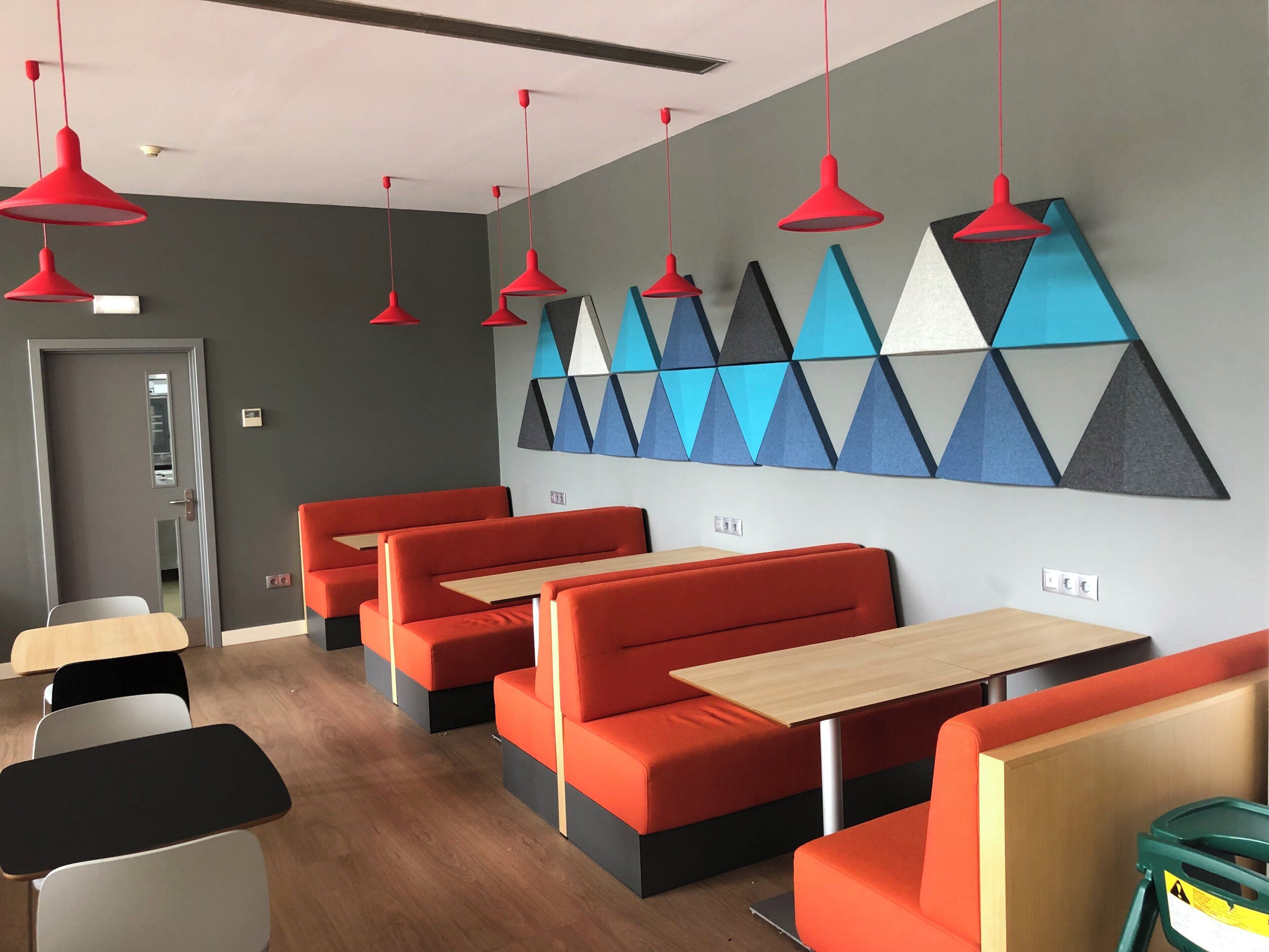 A modern restaurant interior with red booths, wooden tables, and geometric wall art.
