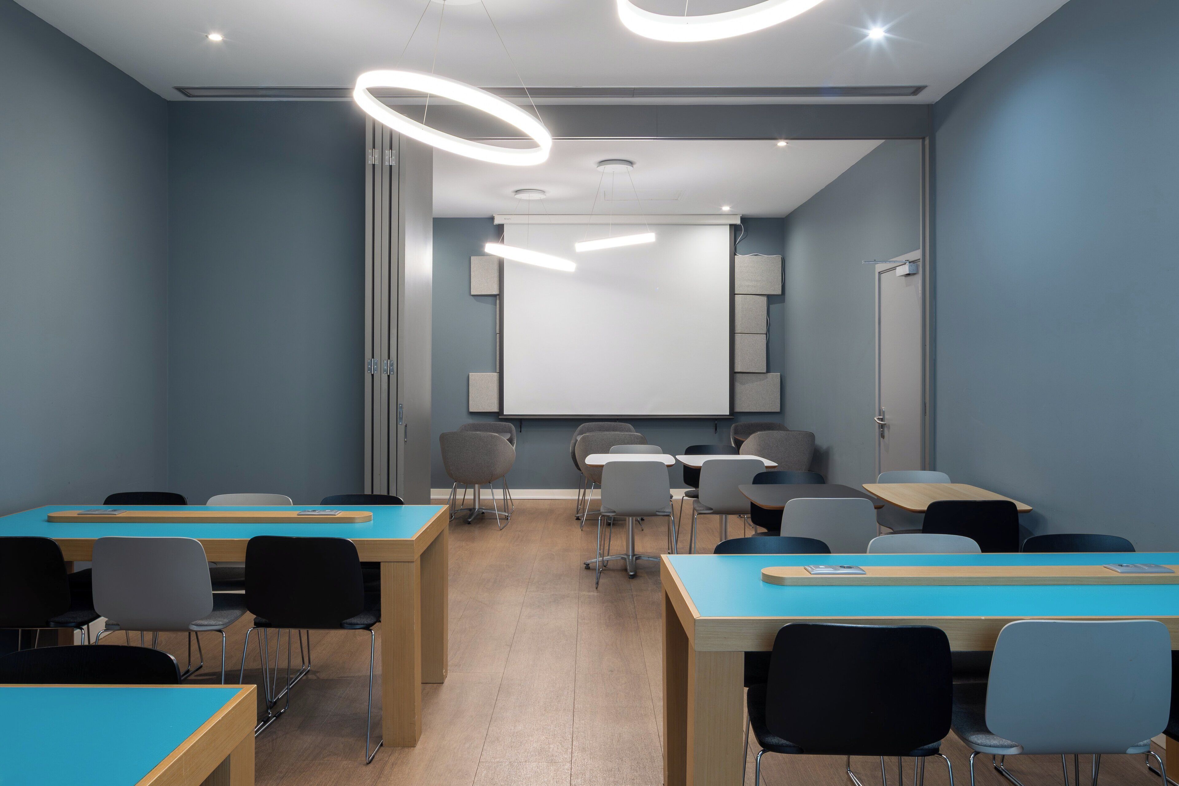 A modern classroom with blue walls, wooden desks, and black chairs.