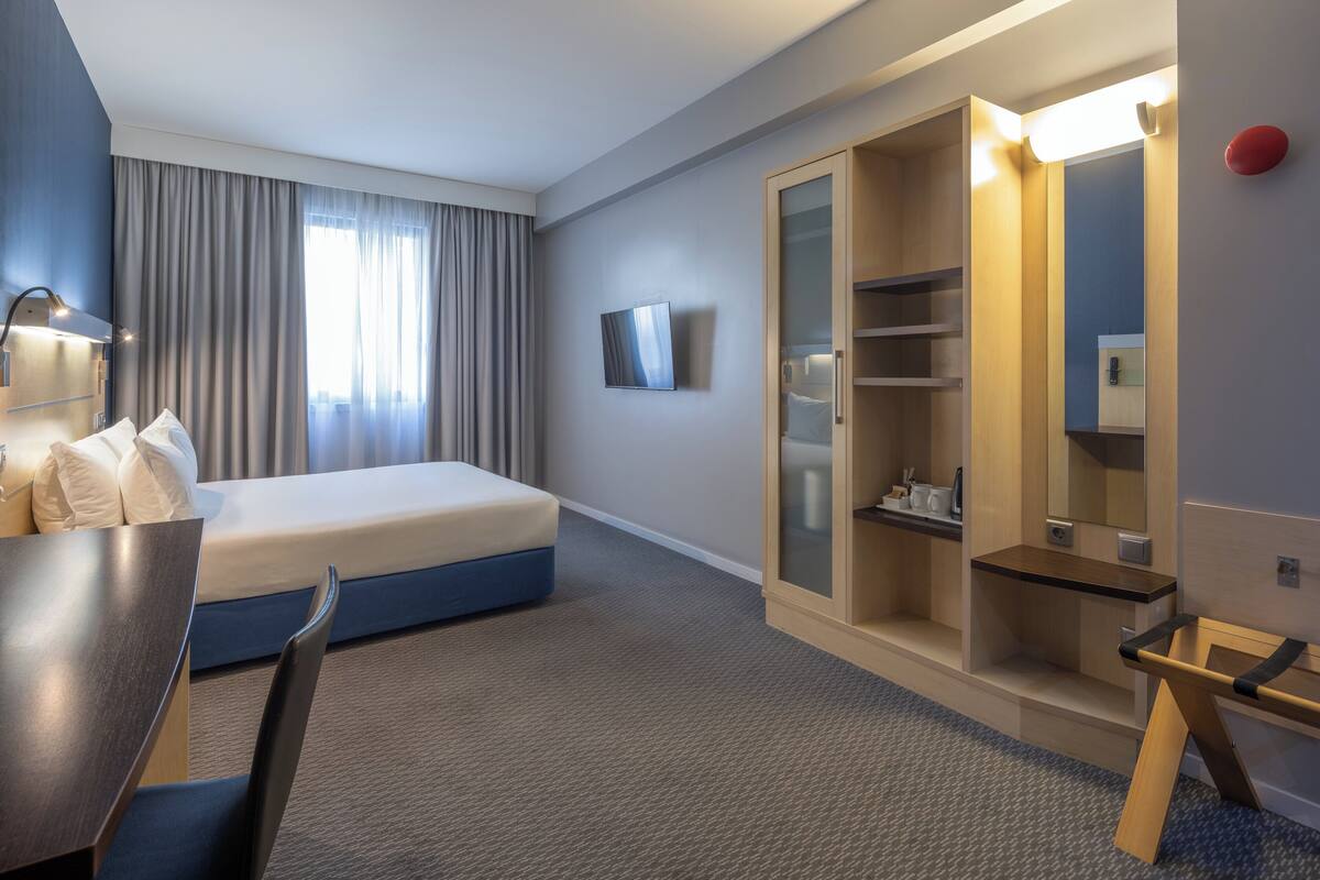 A hotel room with a bed, bedside table, lamp, and a wardrobe with a mirror.
