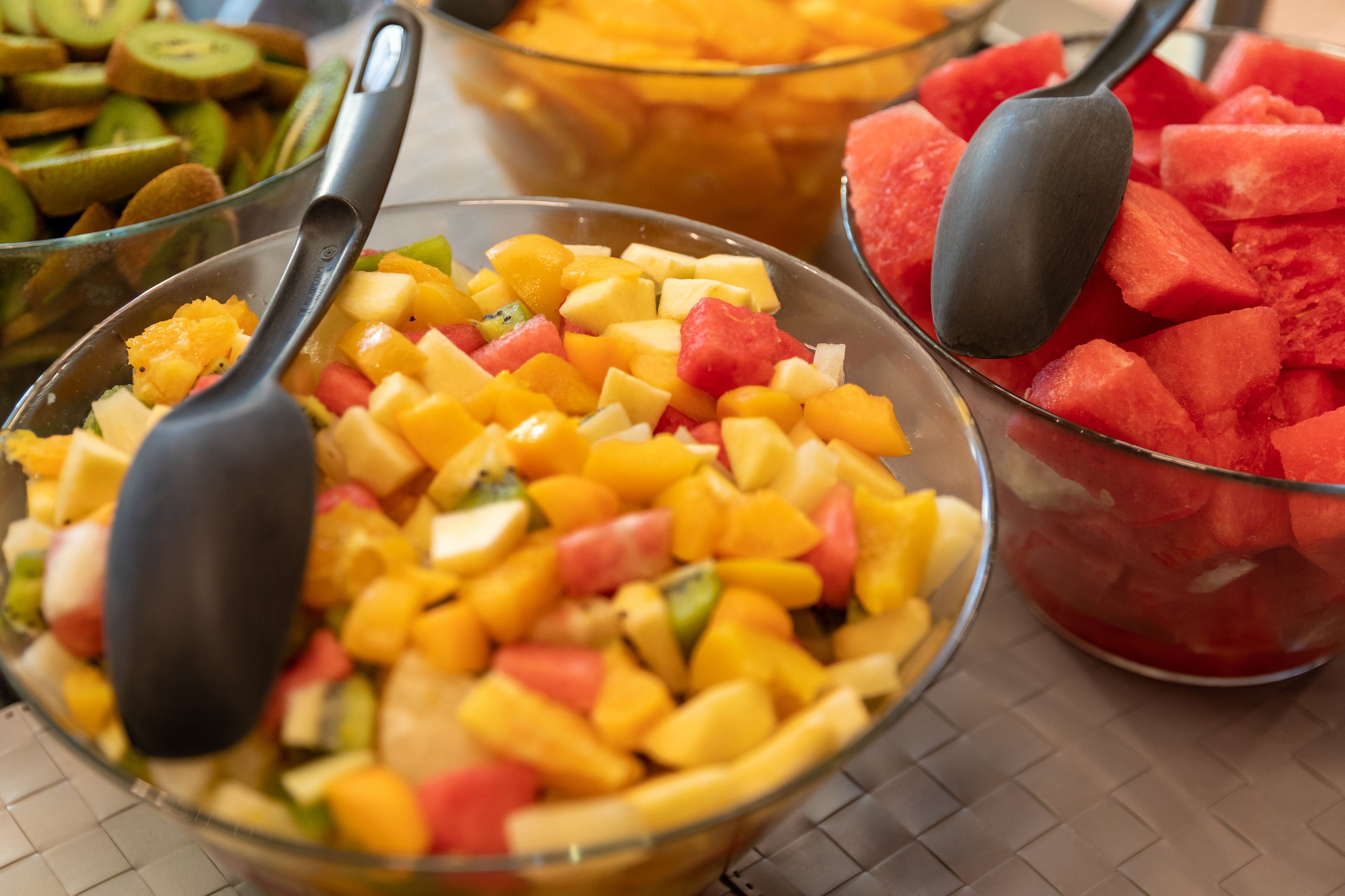Una ciotola di vetro piena di frutta tagliata a cubetti, tra cui mango, mele e kiwi, con un cucchiaio nero.