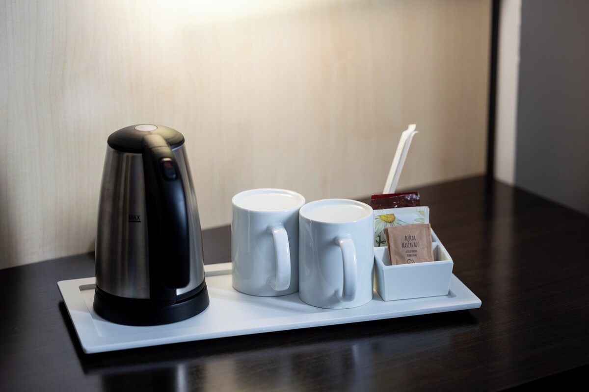 Eine Kaffeestation mit Kaffeemaschine, zwei weißen Tassen, einem Zuckerbehälter und einem Zuckerlätzchen auf einer weißen Tablett.