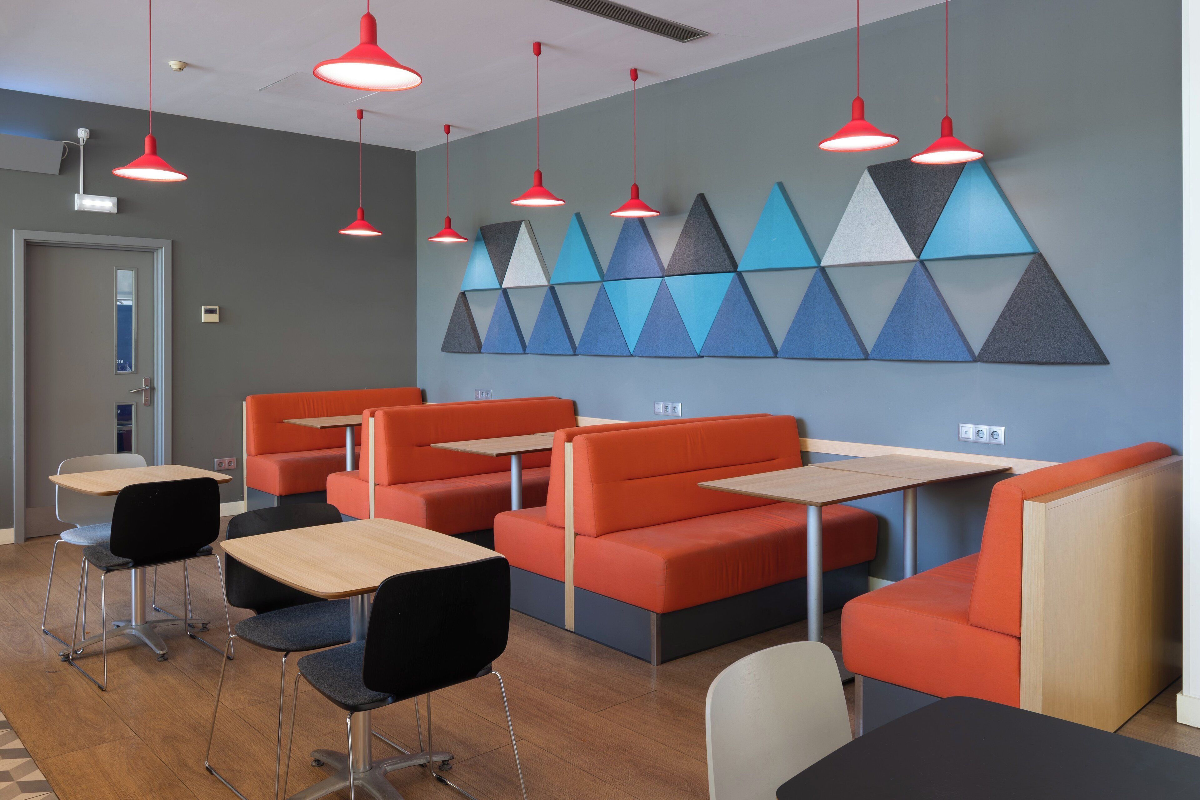 A modern dining area with orange booths, black chairs, and red pendant lights.