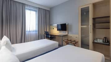 A hotel room with two beds, a desk with a TV, a wardrobe, and a window with curtains.