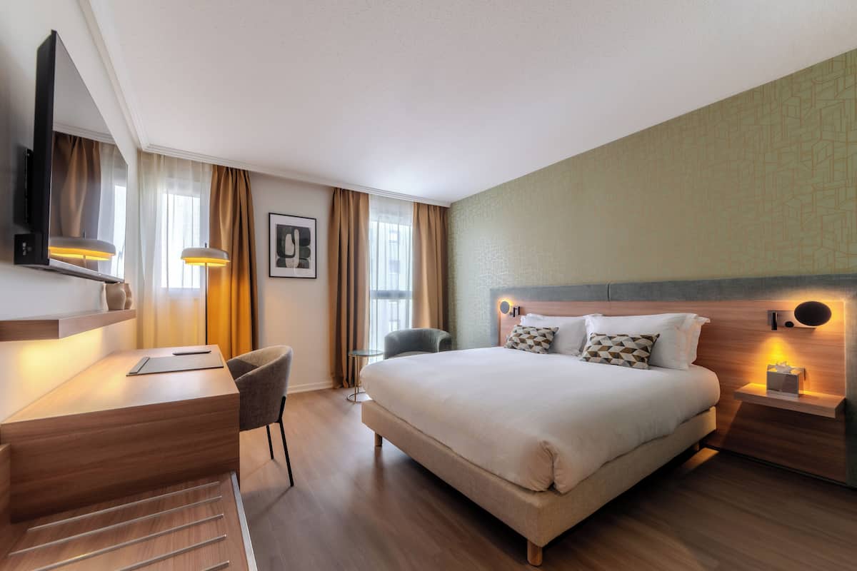 A hotel room with a bed, bedside table, desk, chair, and a TV.