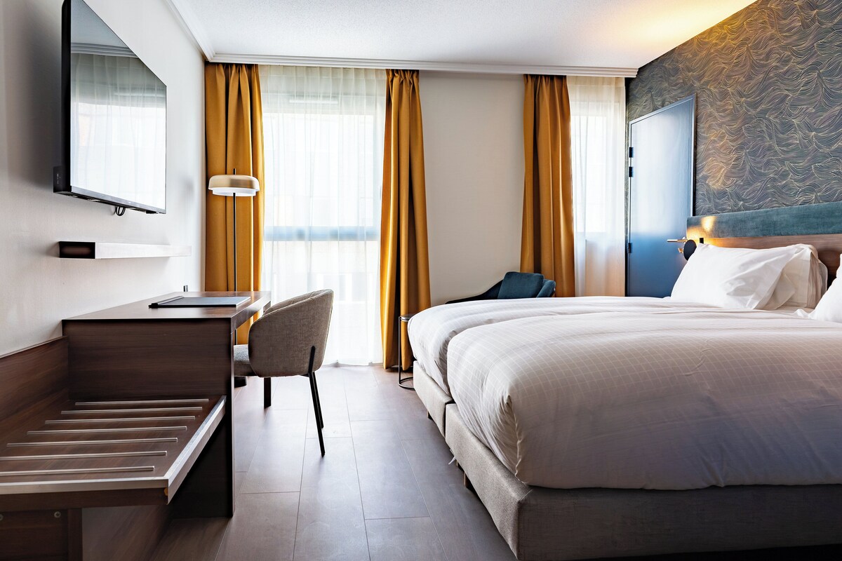 A hotel room with a bed, desk, chair, and a television on the wall.