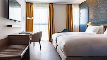 A hotel room with a bed, desk, chair, and a television on the wall.