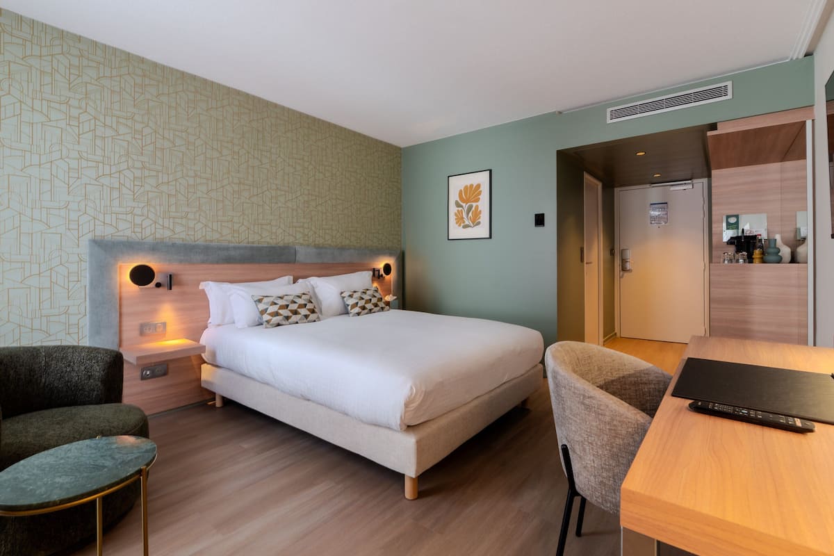 Ein Hotelzimmer mit einem Bett, zwei Sesseln, einem Schreibtisch und einem Fernseher.