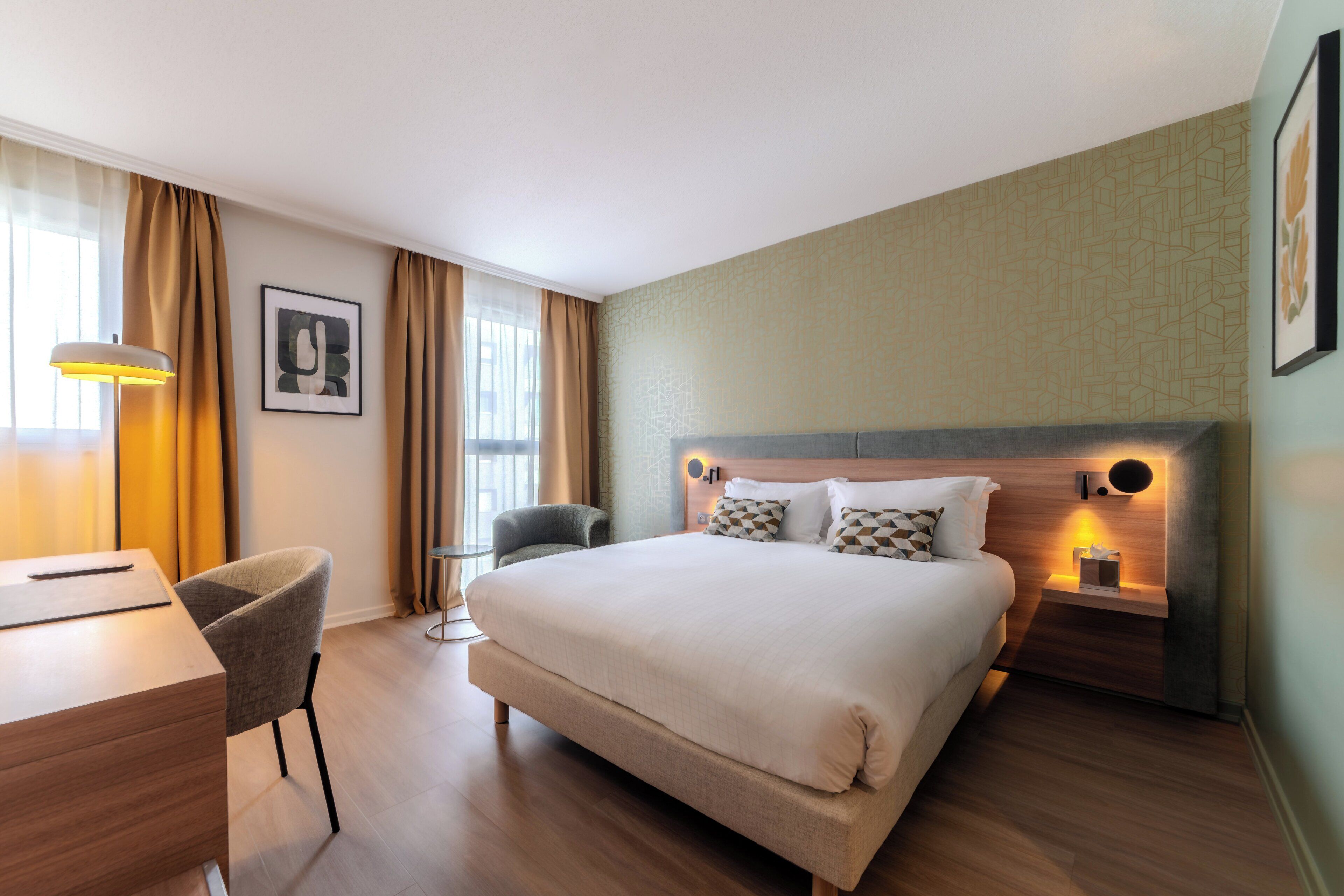 Et hotelværelse med seng, natbord, lampe, stol og skrivebord.