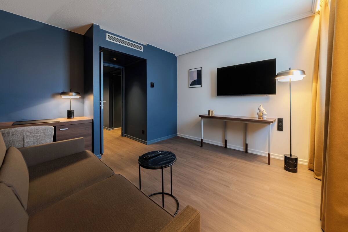 Ein modernes Wohnzimmer mit einer Couch, einem Couchtisch, einem an der Wand montierten Fernseher und einer Lampe.