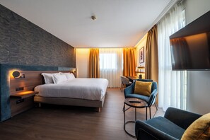 A modern hotel room with a large bed, a desk, a chair, and a television.
