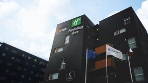 Un bâtiment de l’hôtel Holiday Inn, doté d’une façade noire moderne, de nombreux balcons et de plusieurs drapeaux, dont le drapeau de l’Union européenne.