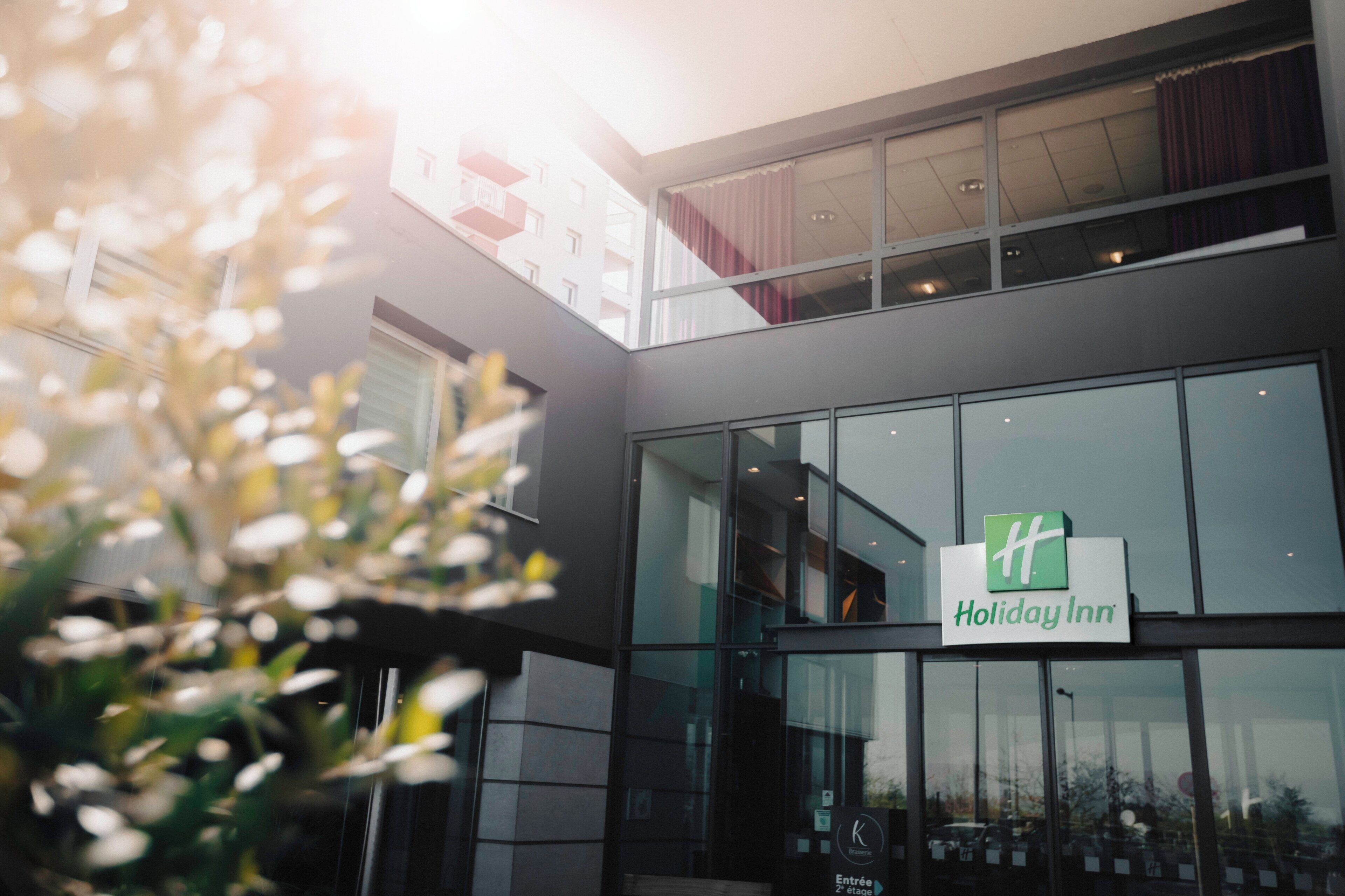 Een Holiday Inn hotel met een moderne glazen gevel, een duidelijke ingang en een balkon op de bovenste verdieping.