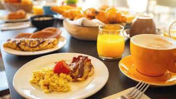 Una mesa de desayuno con platos de comida, un vaso de jugo de naranja y una taza de café.