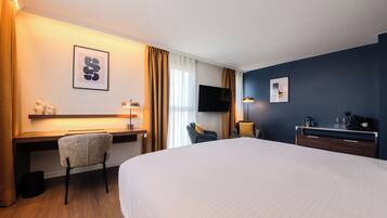 Ein Hotelzimmer mit einem großen Bett, einem Schreibtisch, einem Stuhl, einem Fernseher und einer Schreibtischlampe.