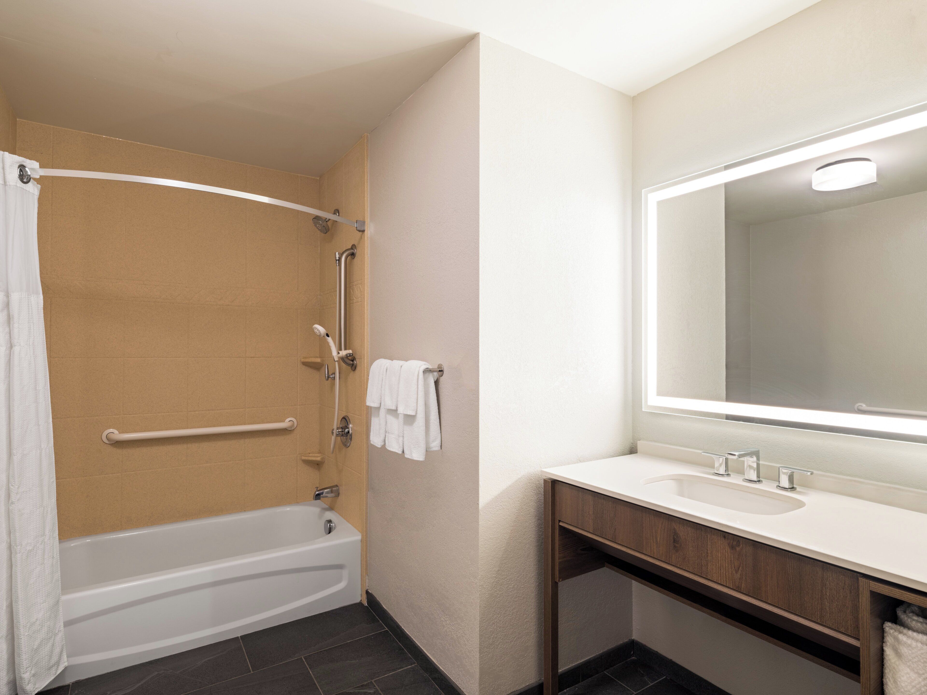 A bathroom with a bathtub, a shower with a grab bar, a sink with a mirror, and a towel rack.