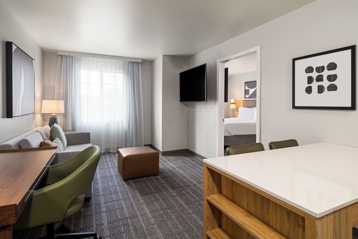 Een hotelkamer met een groot bed, een bureau, een stoel, een bank, een televisie en kunstwerken aan de wanden.