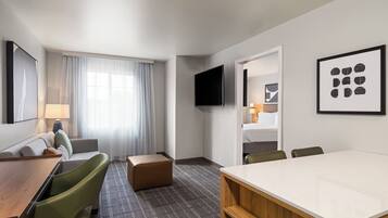 A hotel room with a bed, a desk, a chair, a sofa, a TV, and artwork on the walls.