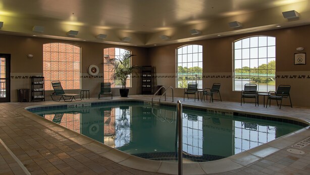 An indoor swimming pool with clear water, surrounded by lounge chairs and a view of a natural landscape.