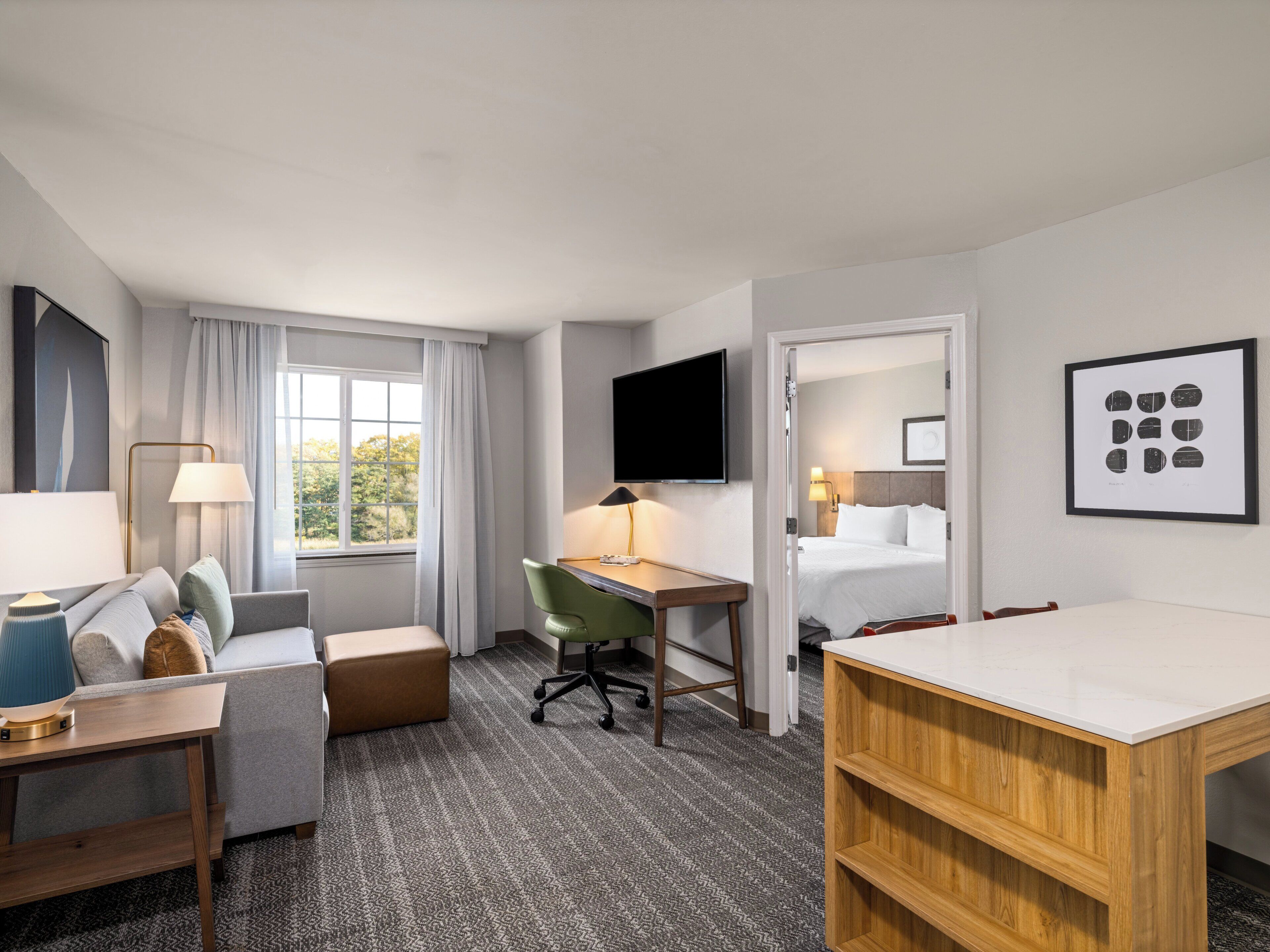 A hotel room with a bed, a desk, a chair, a sofa, a TV, and a window with curtains.