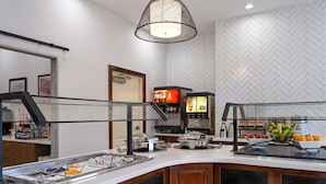A breakfast bar with a variety of food options, a Coca-Cola dispenser, and a coffee machine. - Staybridge Suites Rochester University by IHG (Rochester)
