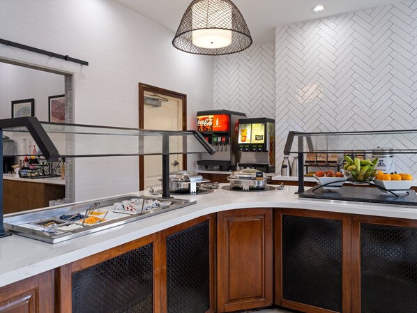 Een ontbijtbuffet met diverse etenswaren, een Coca-Cola automaat en een koffieapparaat.