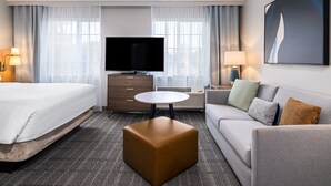 A hotel room with a bed, a sofa, a coffee table, a TV, and a painting on the wall.