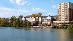 A multi-story hotel with a mix of brick and modern architecture, situated by a lake with trees in the background.