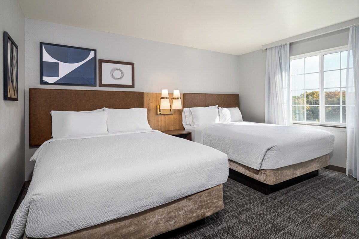 Een hotelkamer met twee bedden, een groot raam met gordijnen en wanddecoratie.