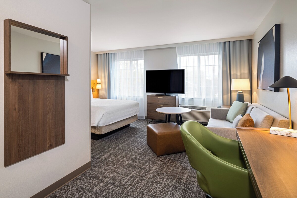 Een hotelkamer met een bed, een televisie, een bureau met stoel, een bank en een groot raam met gordijnen.