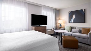 A hotel room with a large bed, a flat-screen TV, a small table, a sofa, and a painting on the wall.