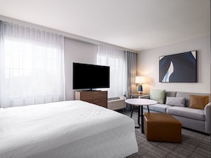 A hotel room with a large bed, a flat-screen TV, a small table, a sofa, and a painting on the wall.