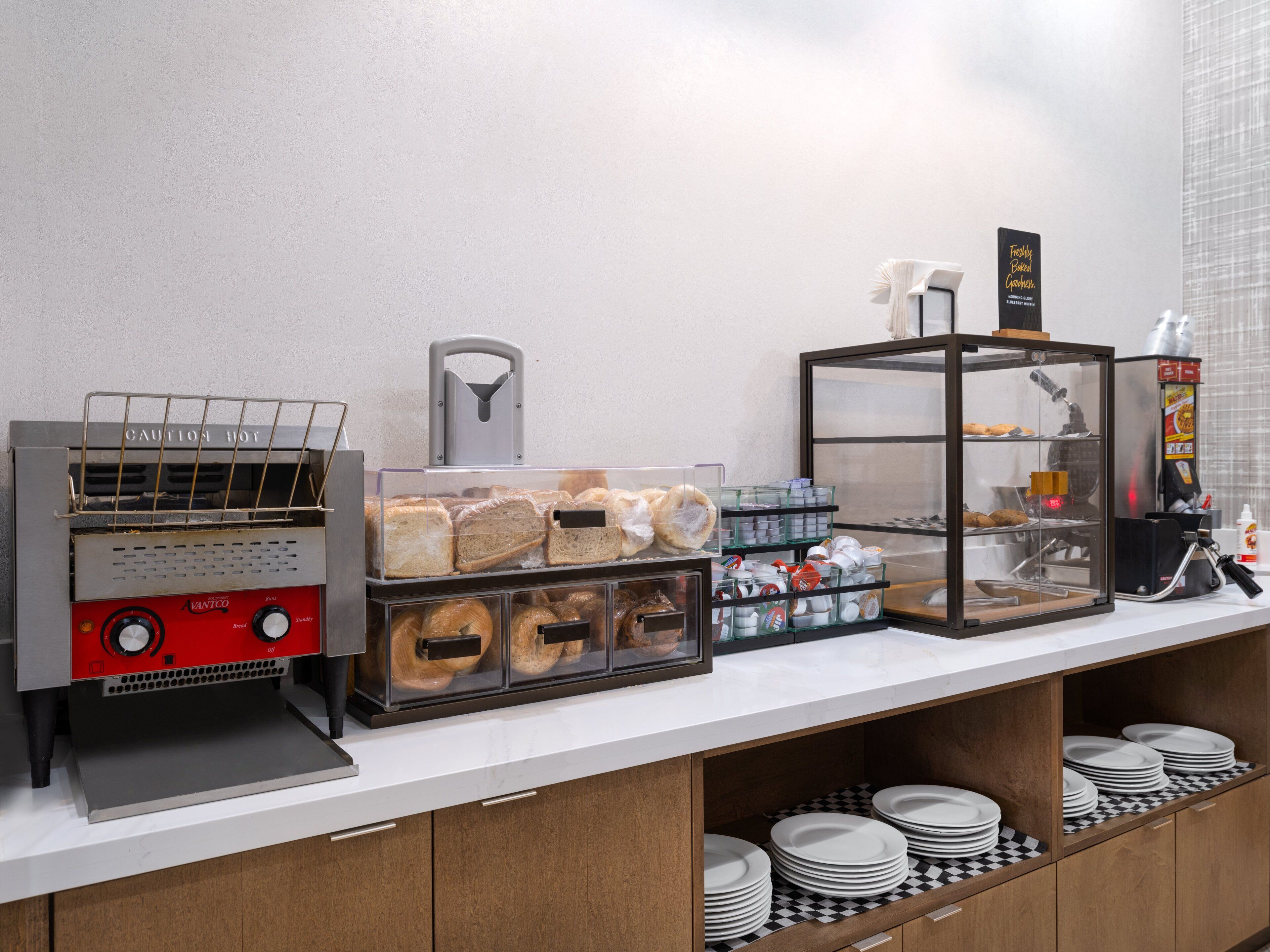 A breakfast bar with a bread display, a coffee machine, and a refrigerated display case.