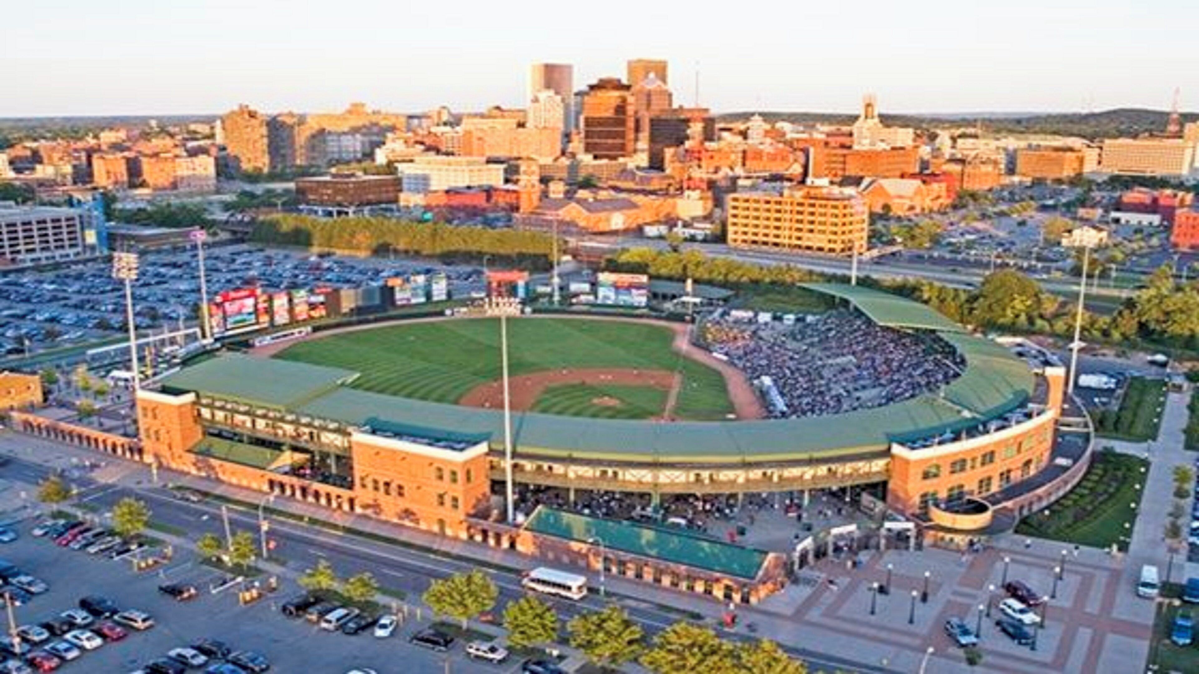 A stadium with a large seating area, surrounded by parking and a cityscape in the background.