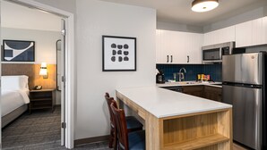 A compact hotel room with a bed, bedside table, lamp, and a small seating area with chairs.