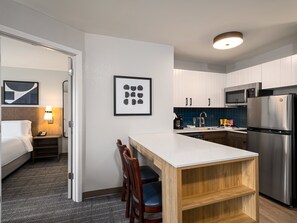 Een compacte hotelkamer met een bed, nachtkastje, lamp en een klein zithoekje met stoelen.