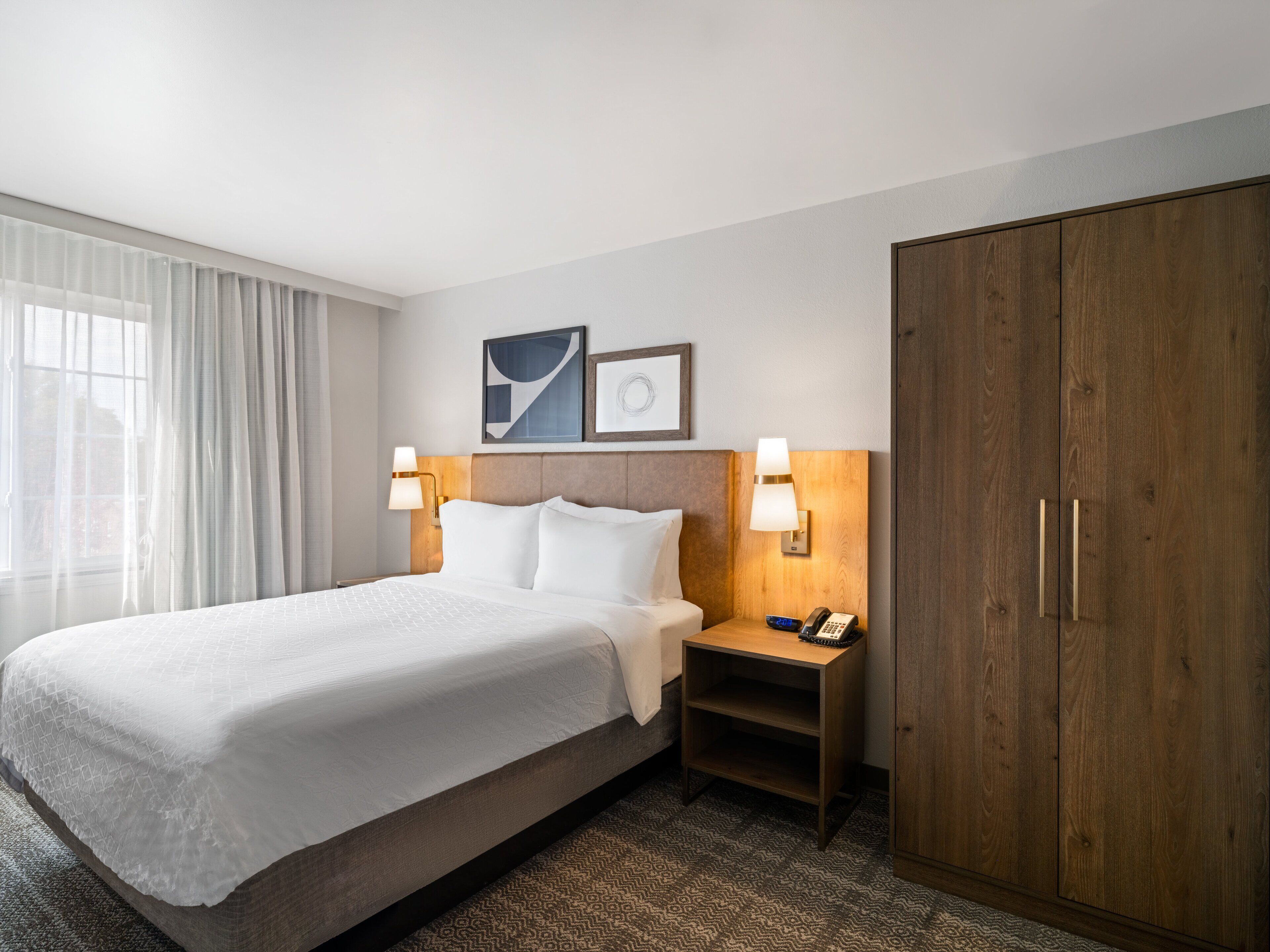 A hotel room with a large bed, two bedside tables with lamps, a wardrobe, and a window with curtains.