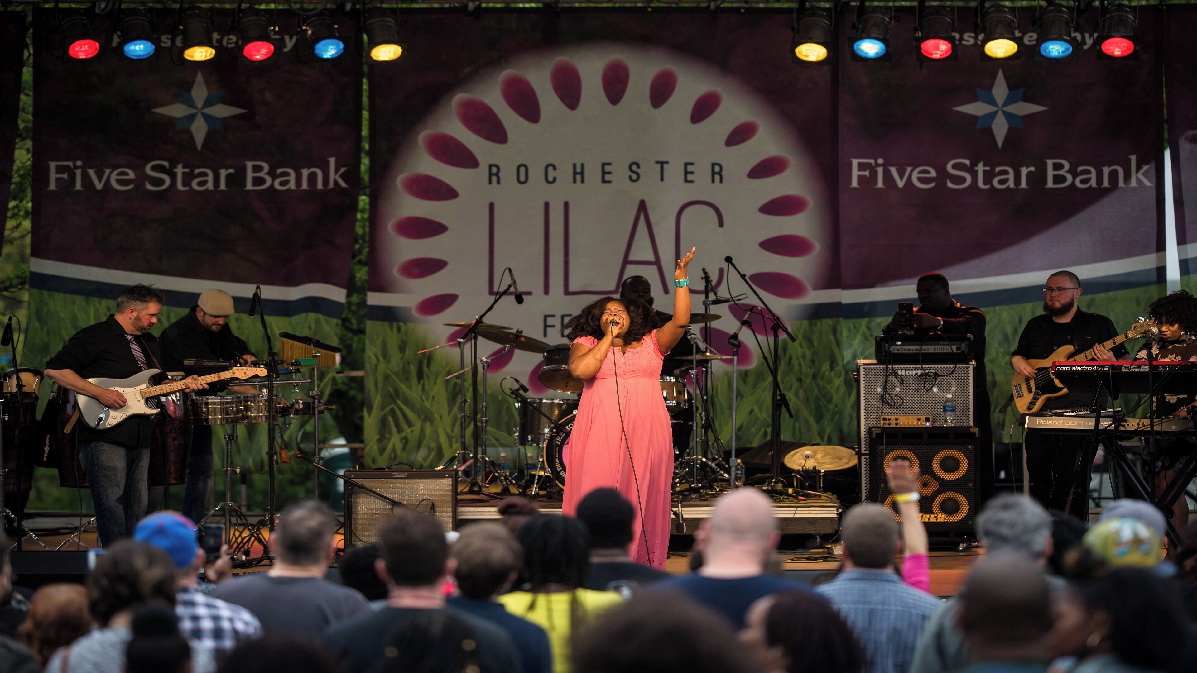 A band performing on stage with a banner reading 'ROCHESTER LILAC' and 'Five Star Bank' in the background.
