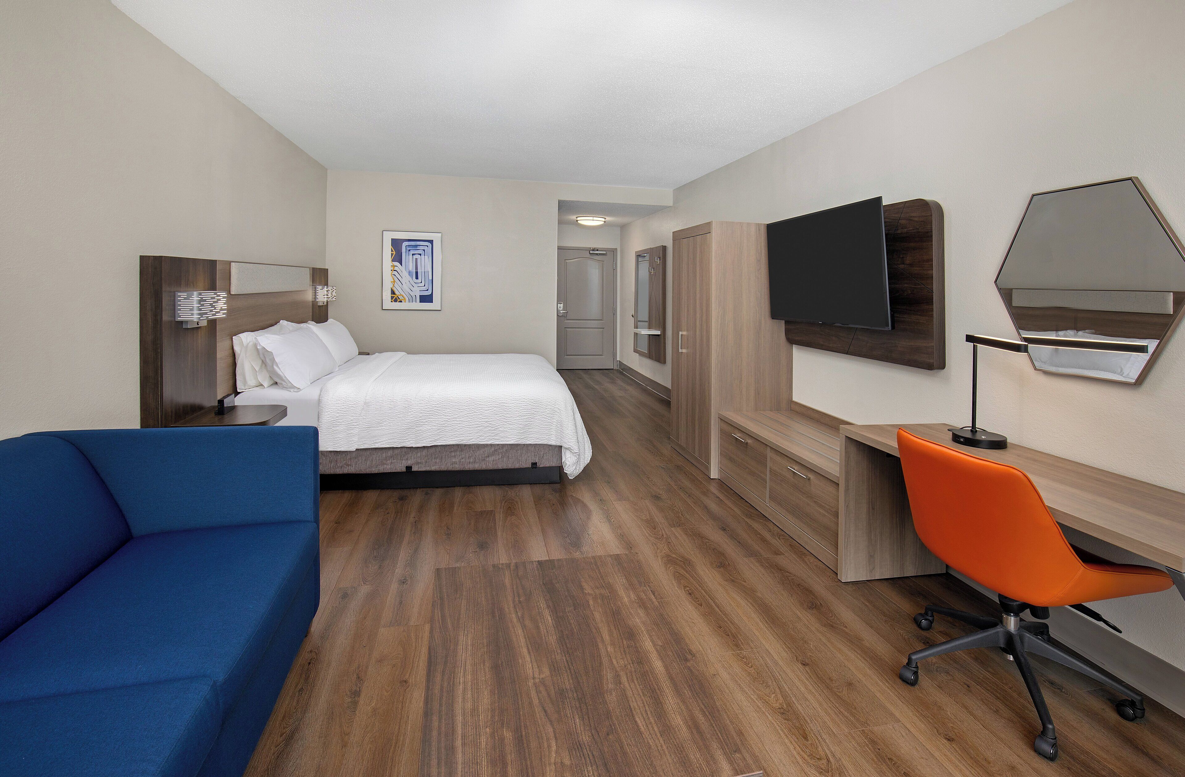 Habitación de hotel con cama, escritorio, silla, televisor y armario.